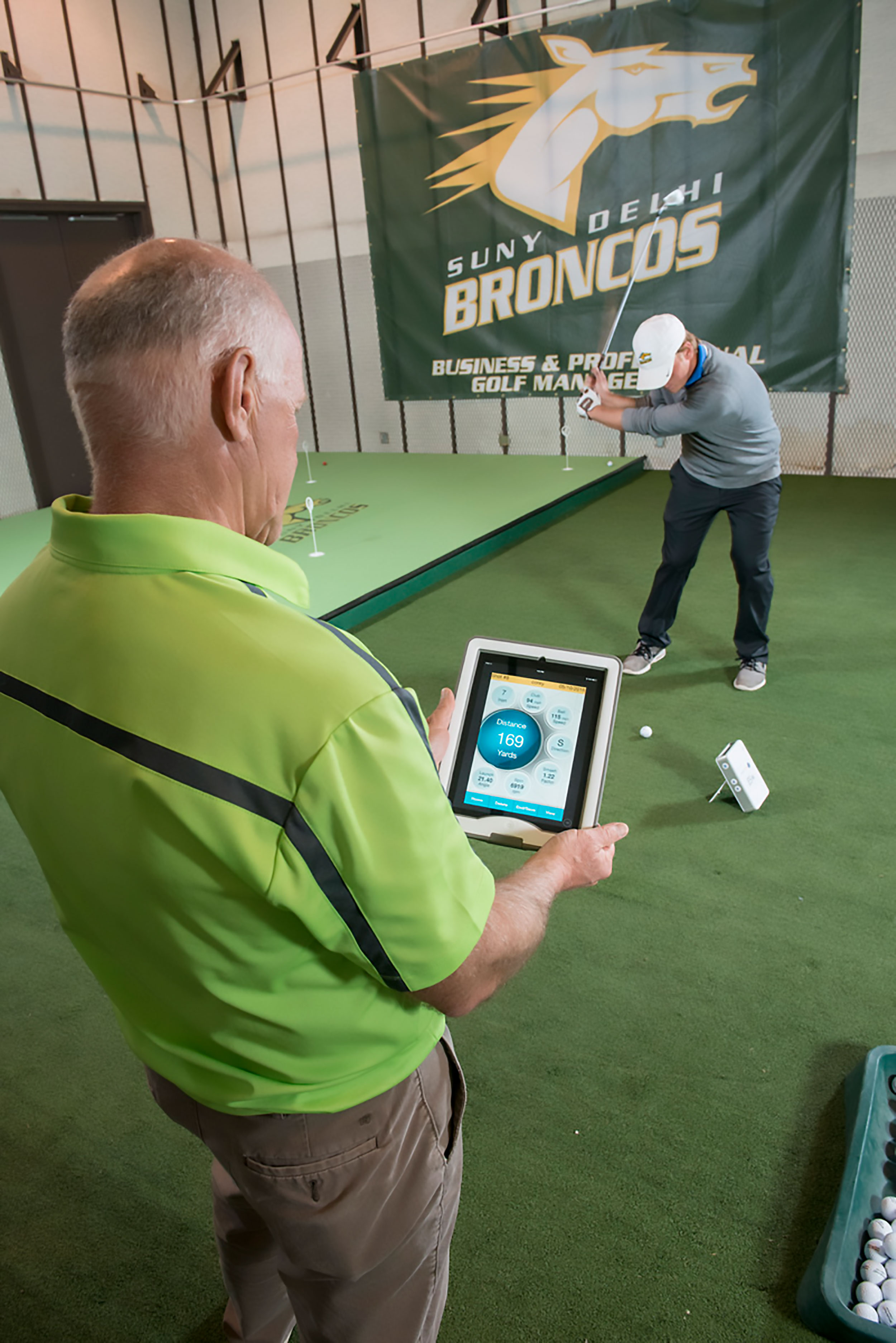 Student in golfing indoors with professor looking at tablet