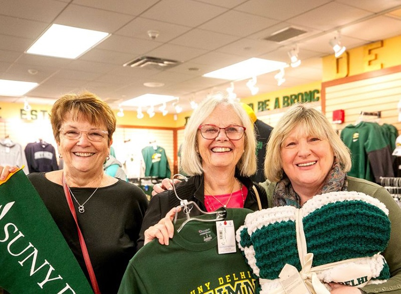 Three SUNY Delhi alumni smile and show Delhi swag in the campus bookstore