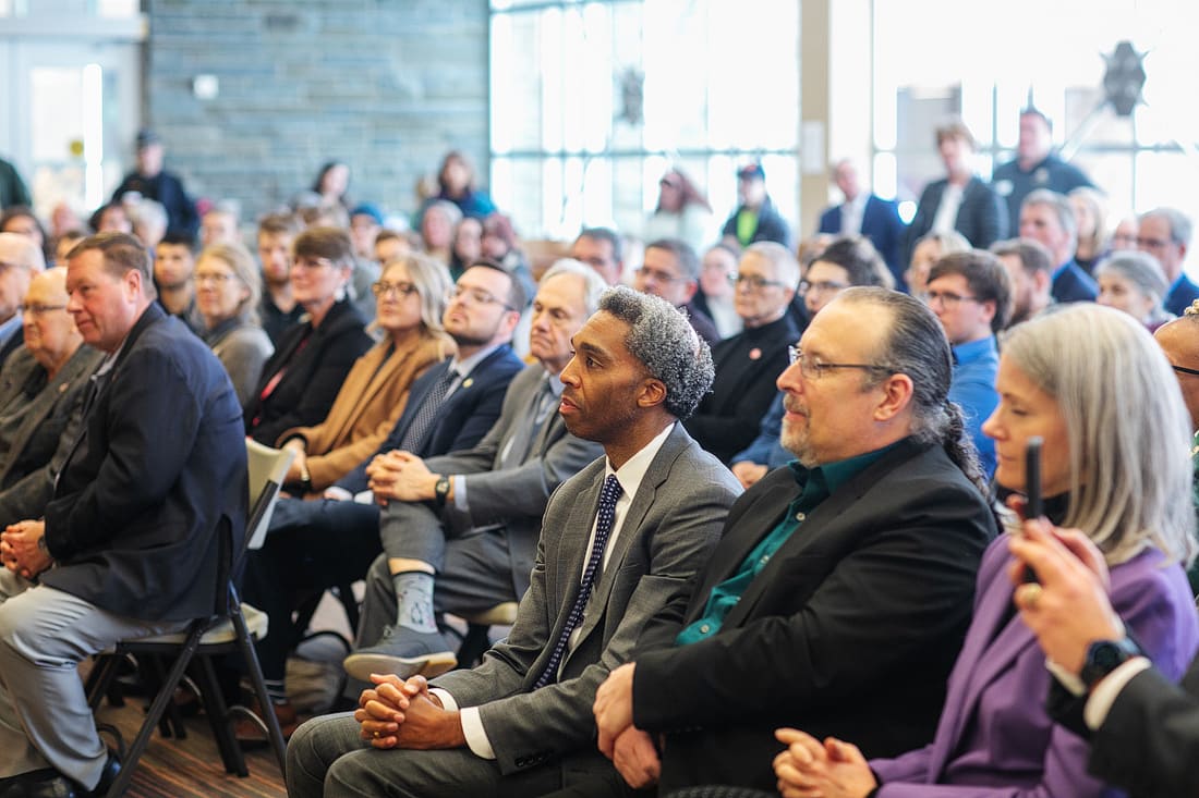 A large group of people sit attentively in rows at an indoor event or conference, facing a speaker outside the frame.