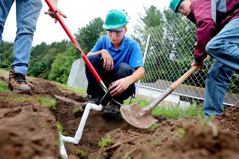 Student inspecting plumbing in ground