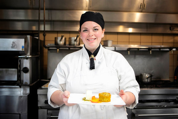 Alum Carly Yezzo holding tray of food in kitchen