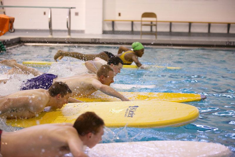 Student paddling on surf boards in swimming pool