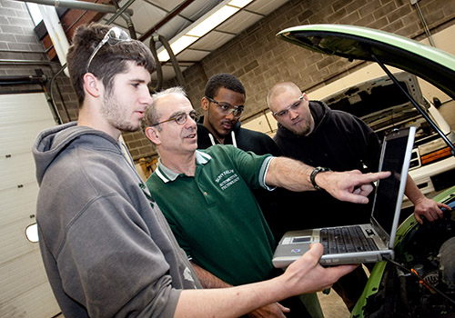 Students and instructor working on a laptop connected to a car