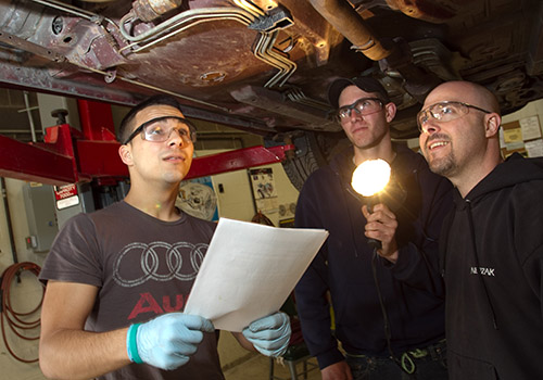 Students standing under a car on a lift