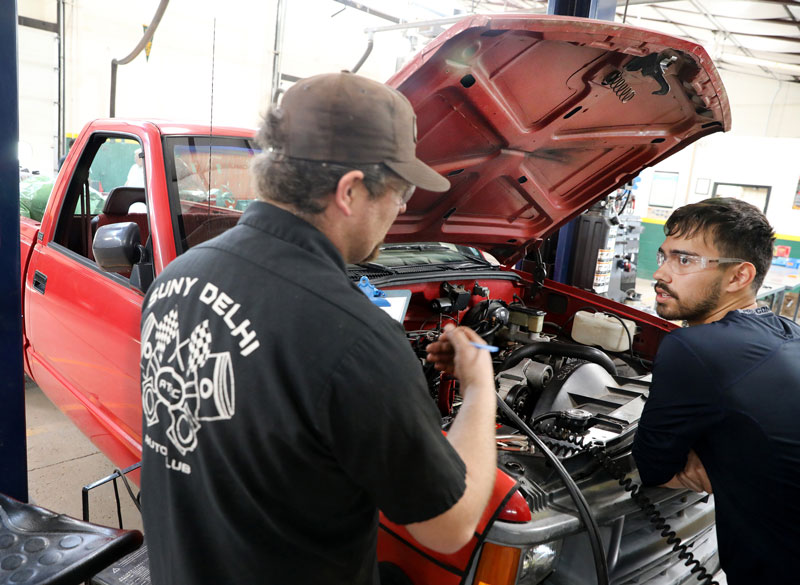 Automotive student and faculty working on car in auto lab