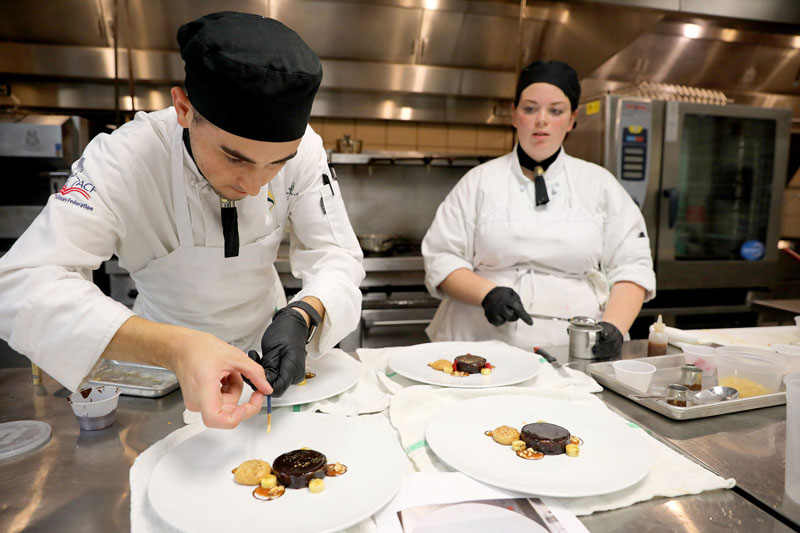 Two culinary students preparing food in kitchen