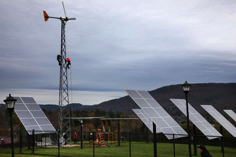 Students climbing wind turbine alongside solar panels