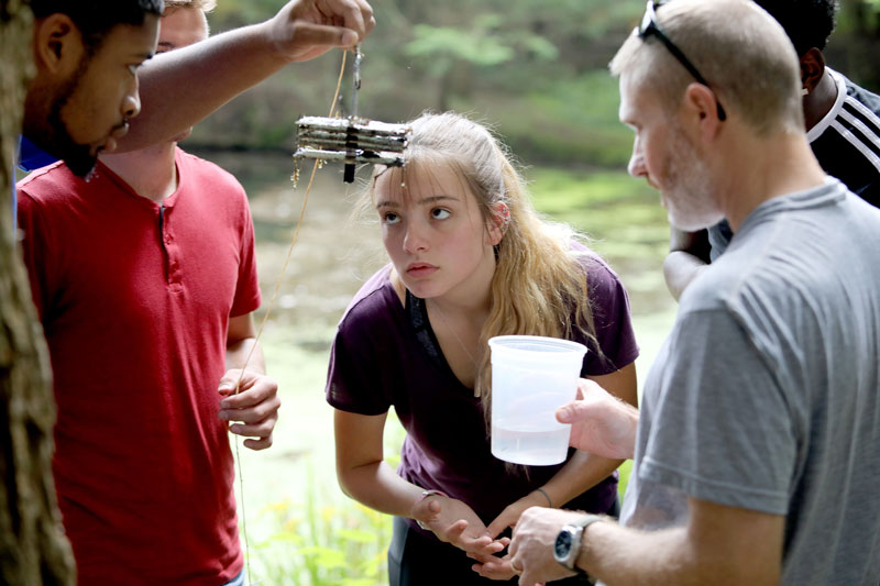 Students studying specimen outdoors with faculty