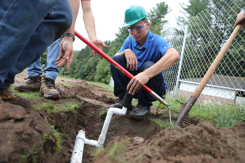 Students examining pipes in ground