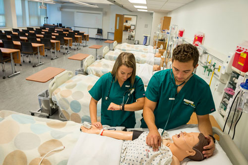 Nursing students practicing skills on mannequin in bed