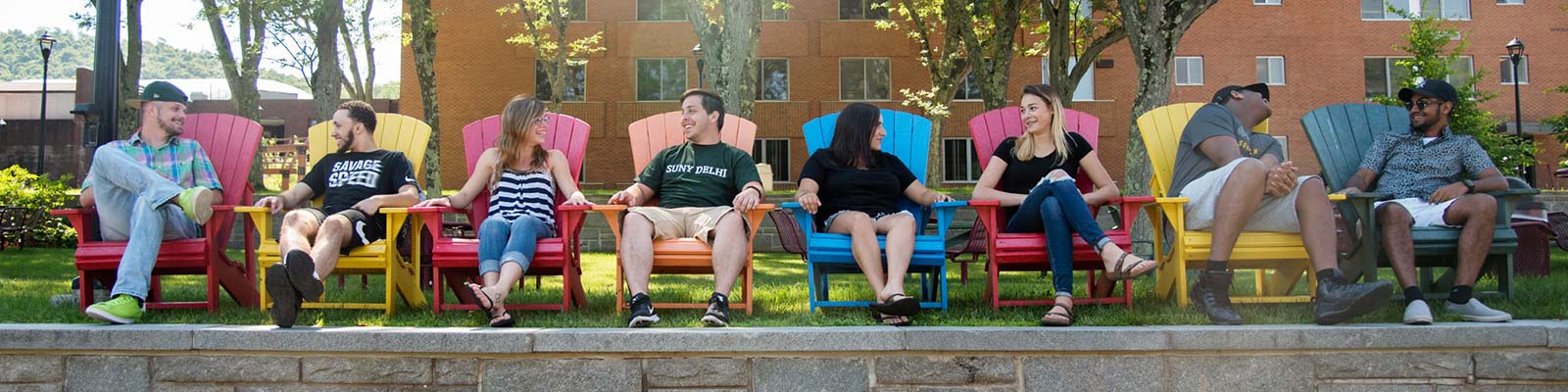 Students relaxing in front of a dorm in Adirondack chairs