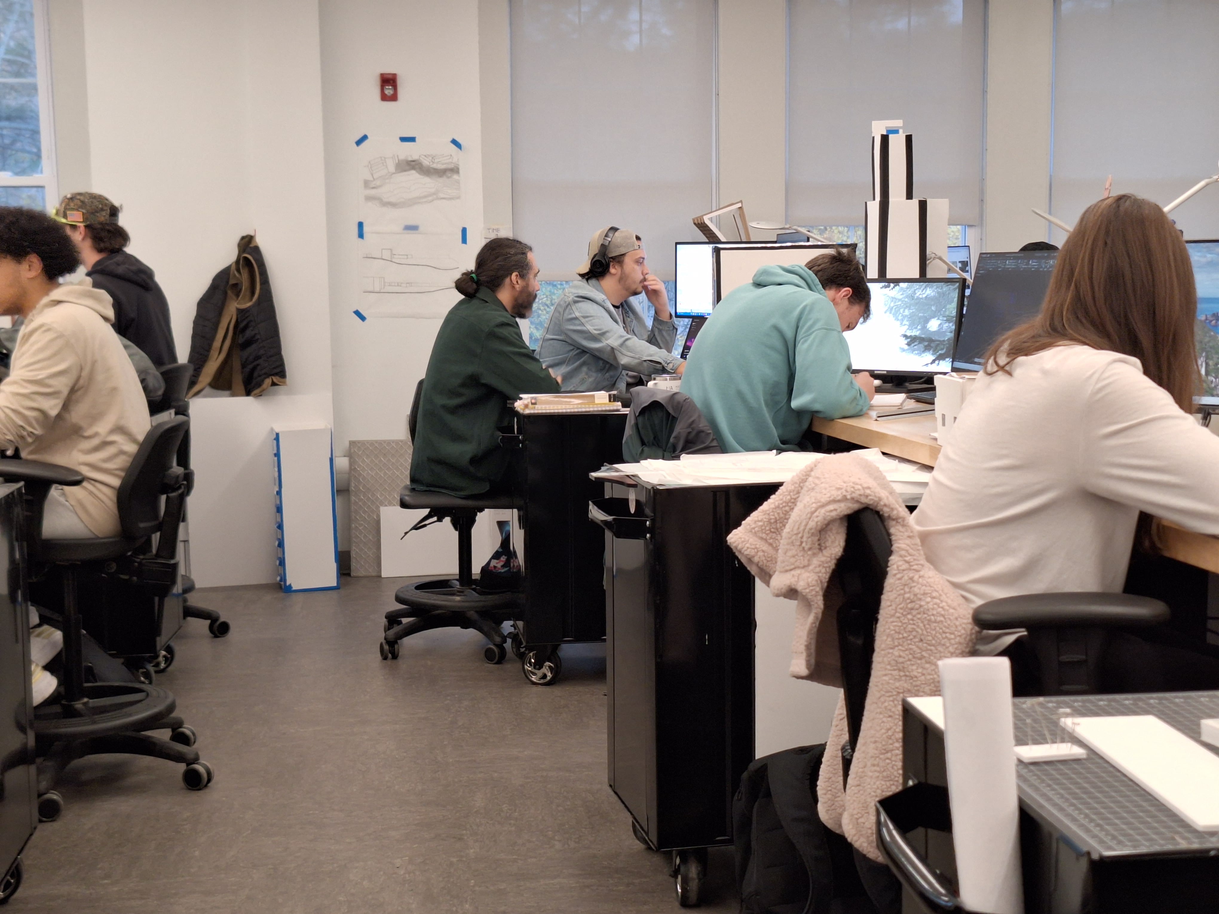 Architecture majors at SUNY Delhi work on computers in a modern studio with large windows and architectural drawings.